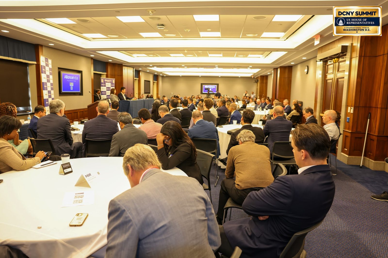 Guests seated at round tables in a long conference room, seen from the side