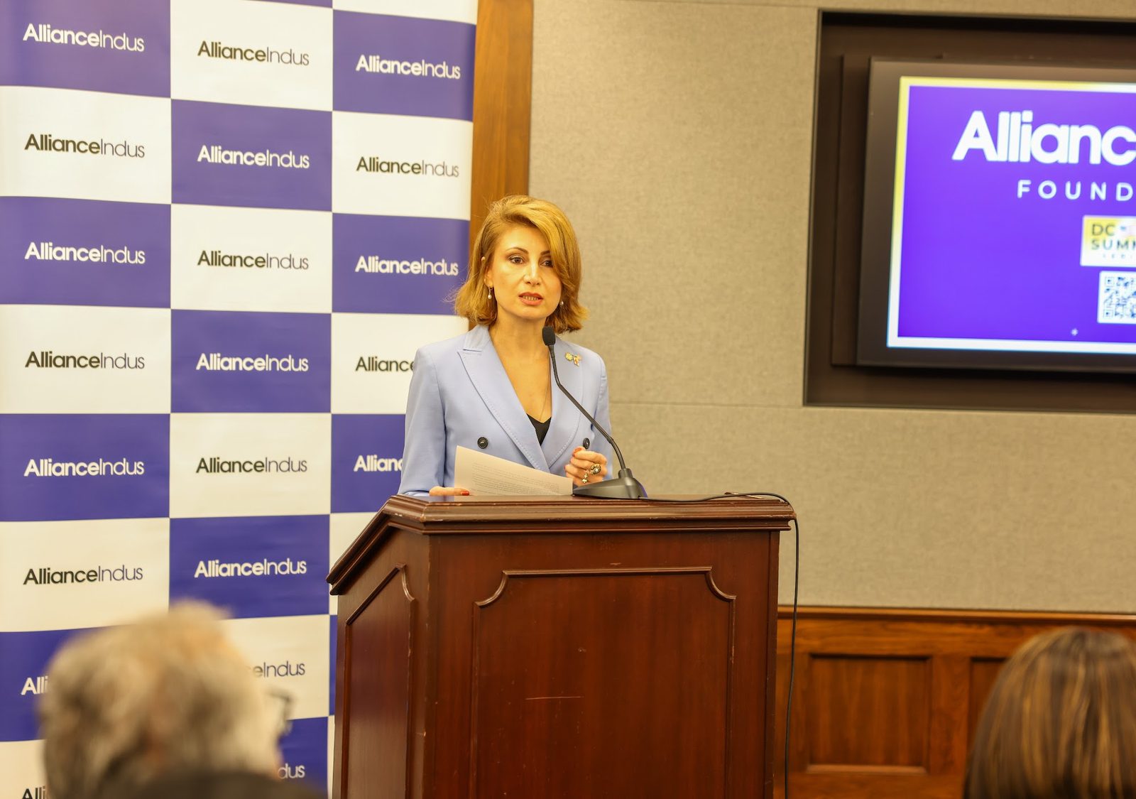 Ambassador Tamar Taliashvili reads remarks at a wooden podium in front of an AllianceIndus backdrop