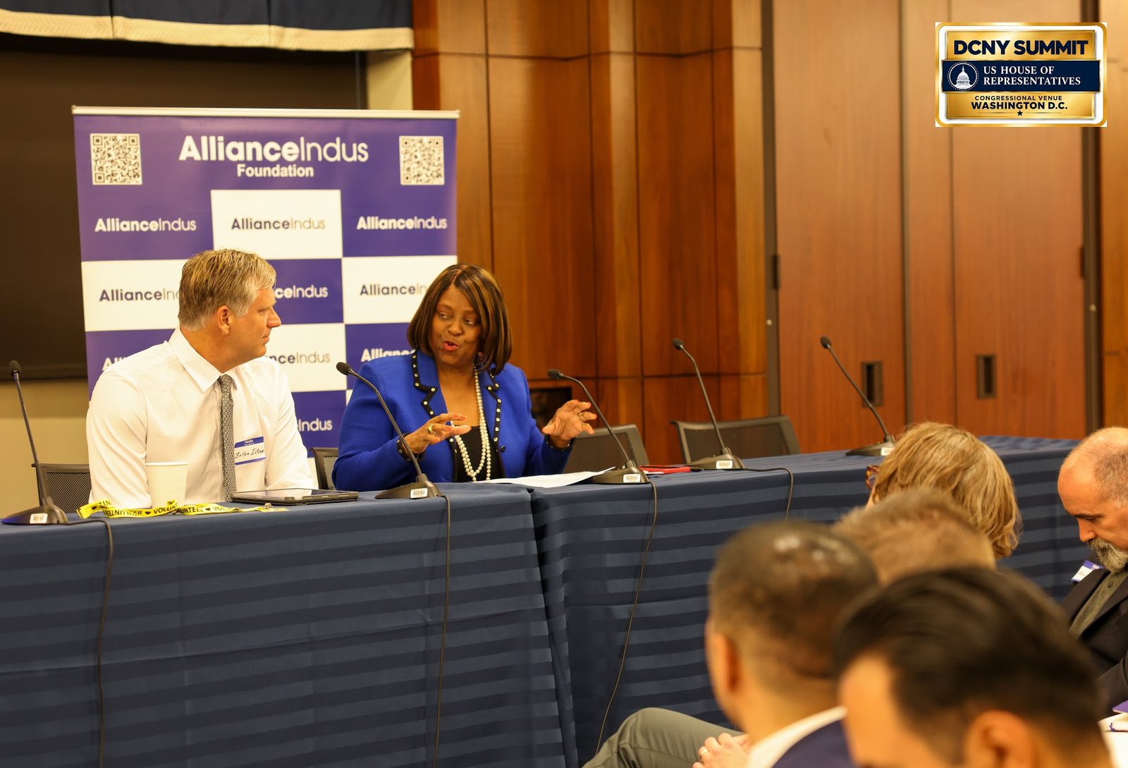 Two panelists in conversation at a draped table in front of an AllianceIndus banner