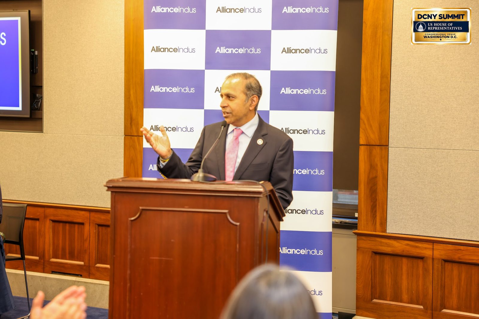 Rep. Raja Krishnamoorthi, in a pink tie, gestures while speaking at the podium