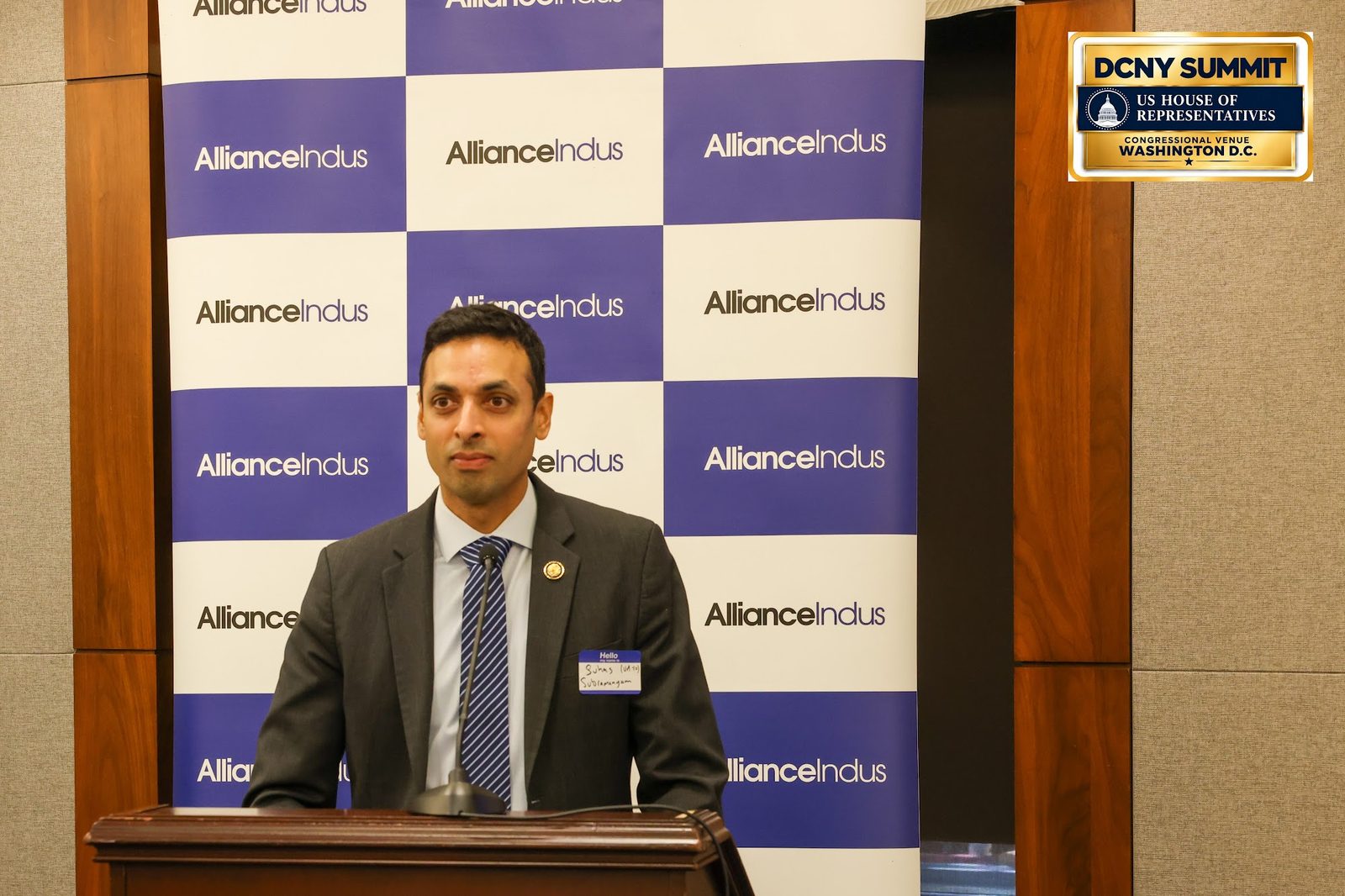 Rep. Suhas Subramanyam speaks at the podium in front of an AllianceIndus backdrop