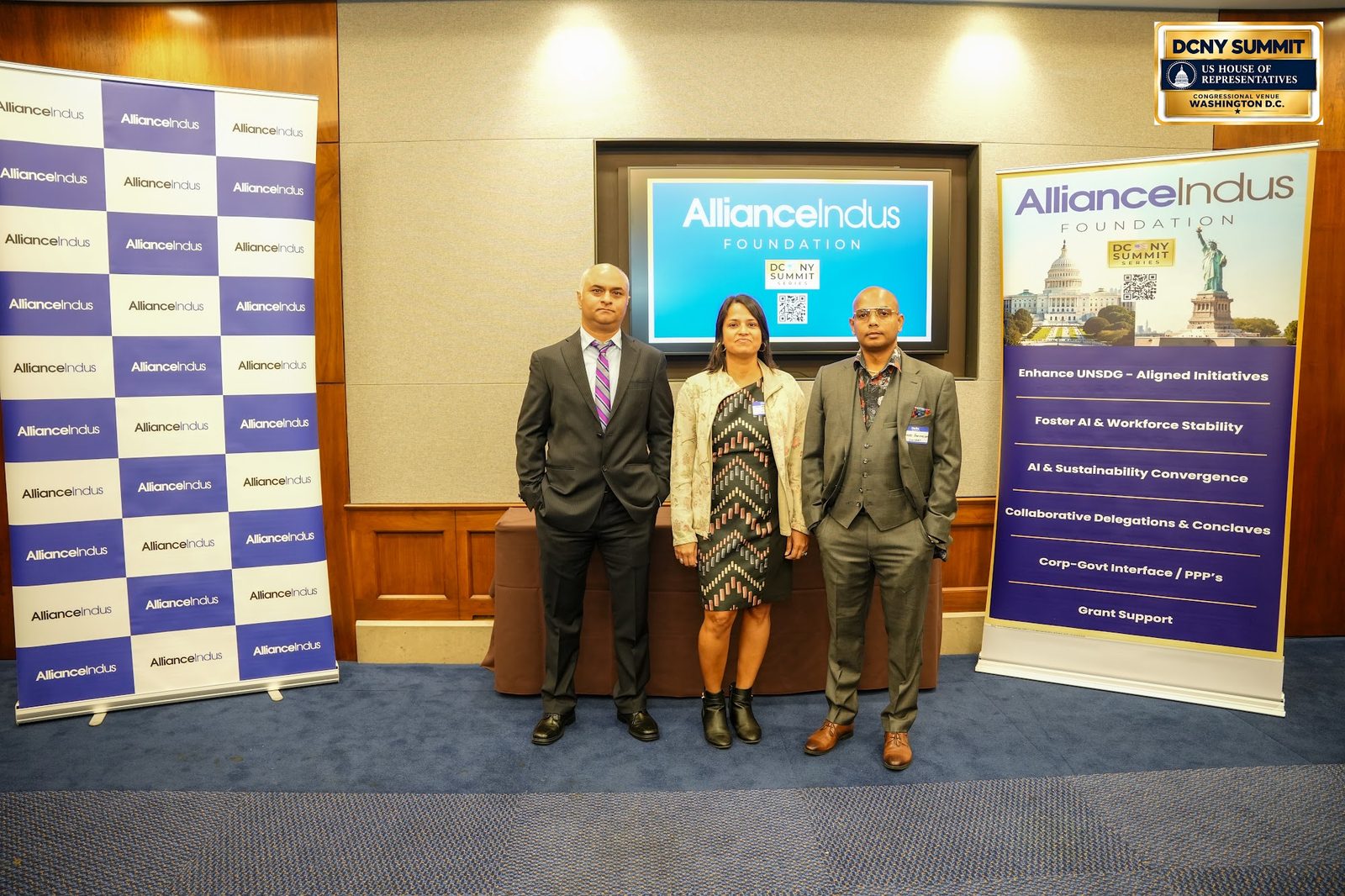 Three guests pose in front of the AllianceIndus backdrop and banner