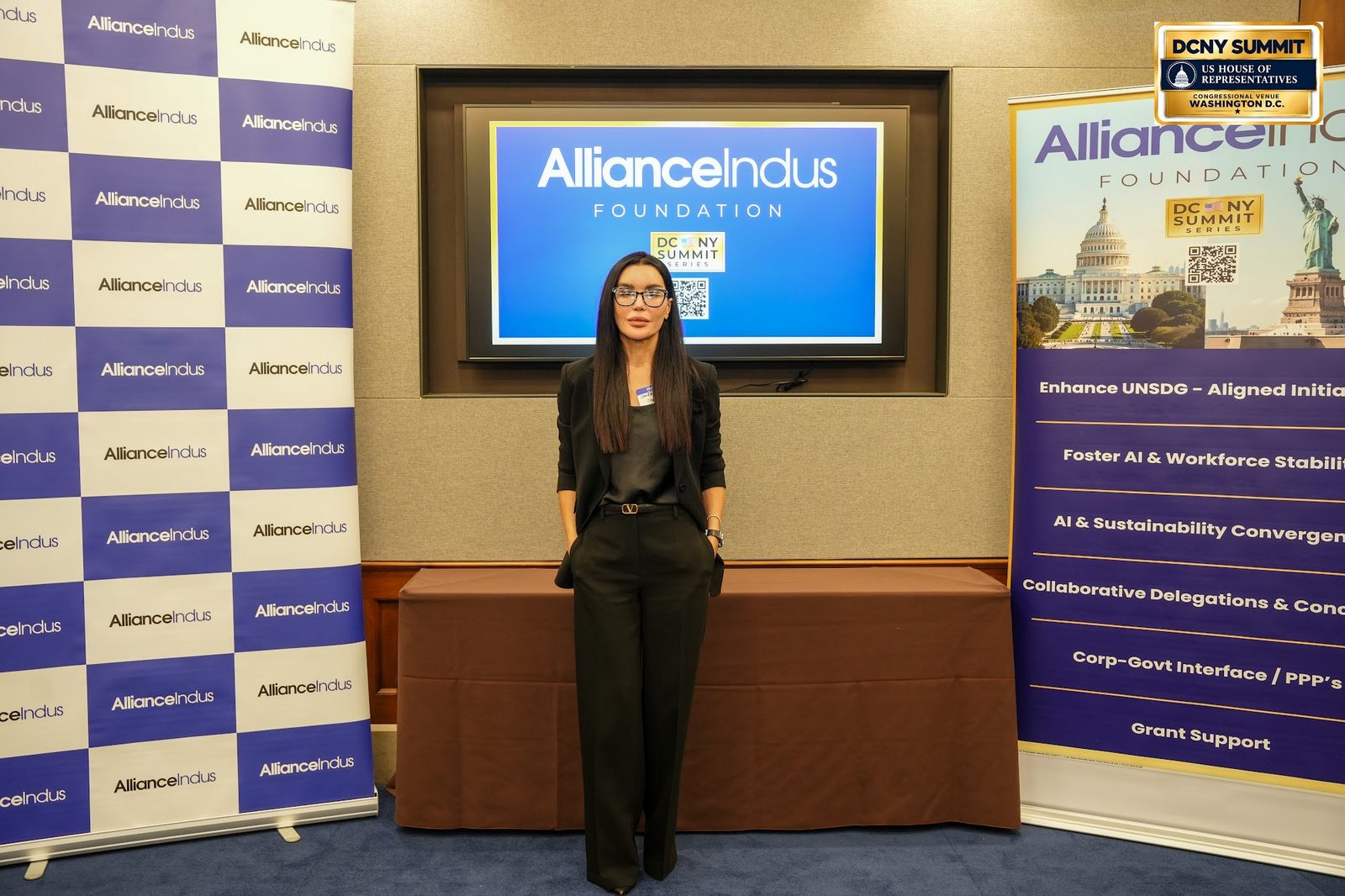 A woman in black poses at the AllianceIndus photo wall