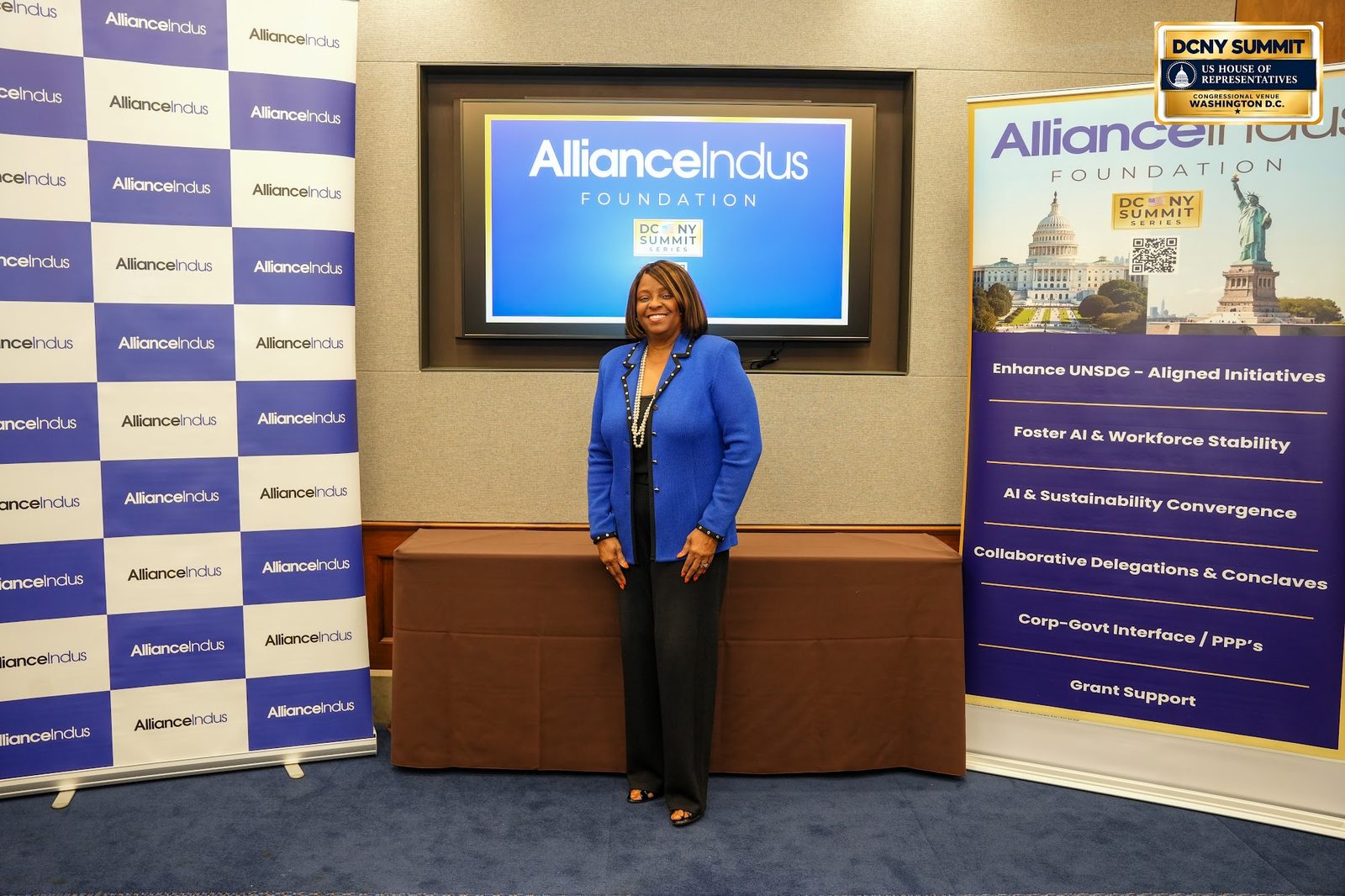 A woman in a blue jacket poses at the AllianceIndus photo wall