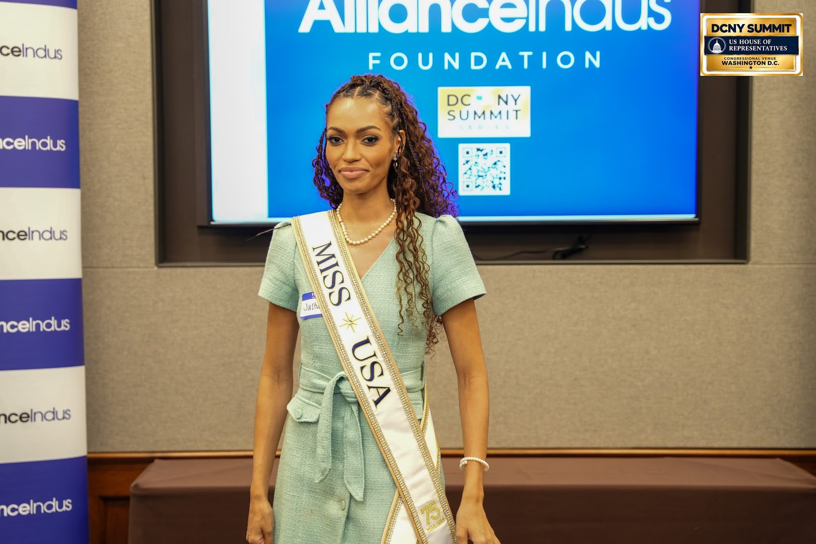 A woman wearing a Miss USA sash stands at the AllianceIndus photo wall