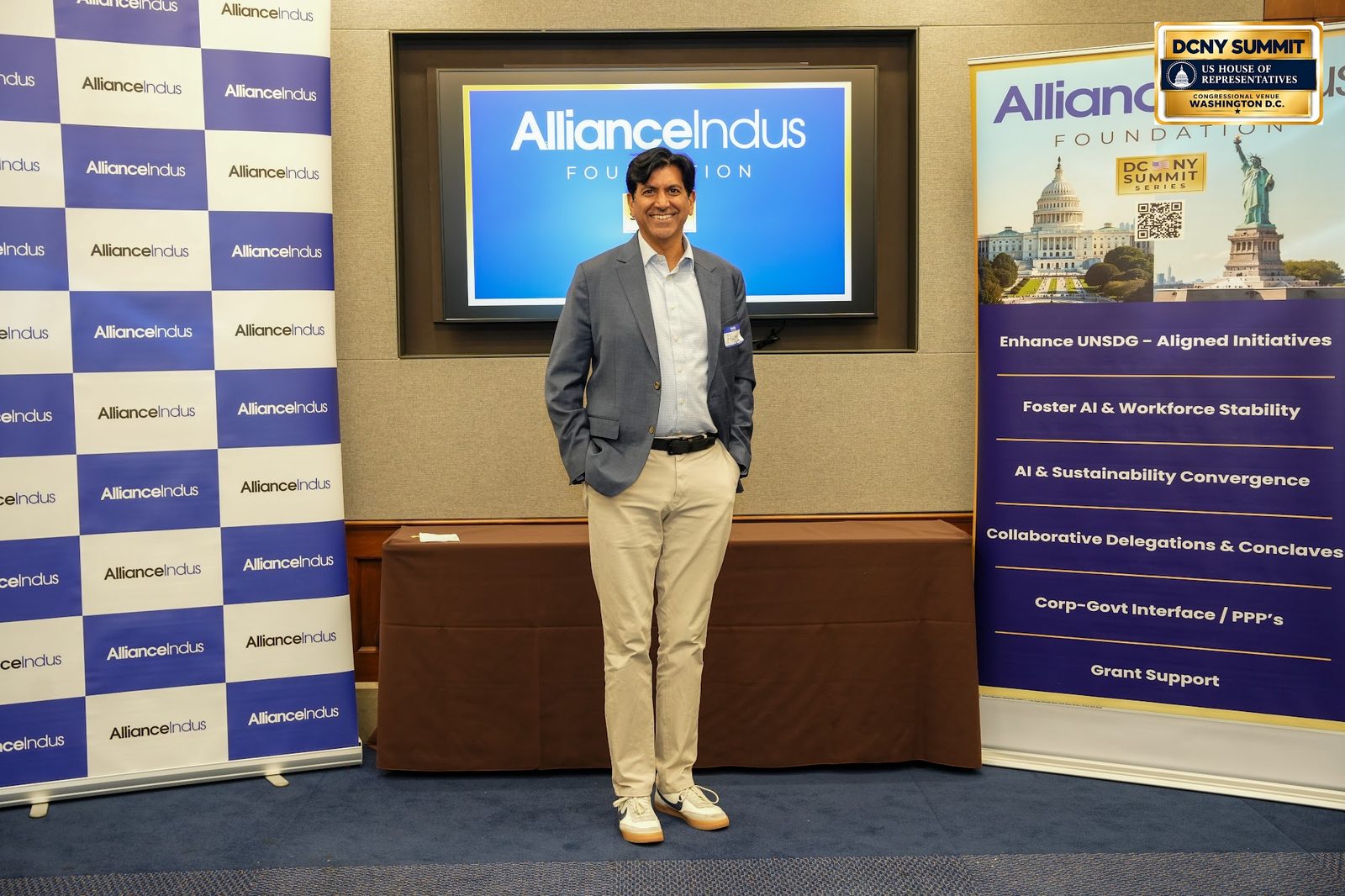 A man in a blazer and light trousers poses at the AllianceIndus photo wall