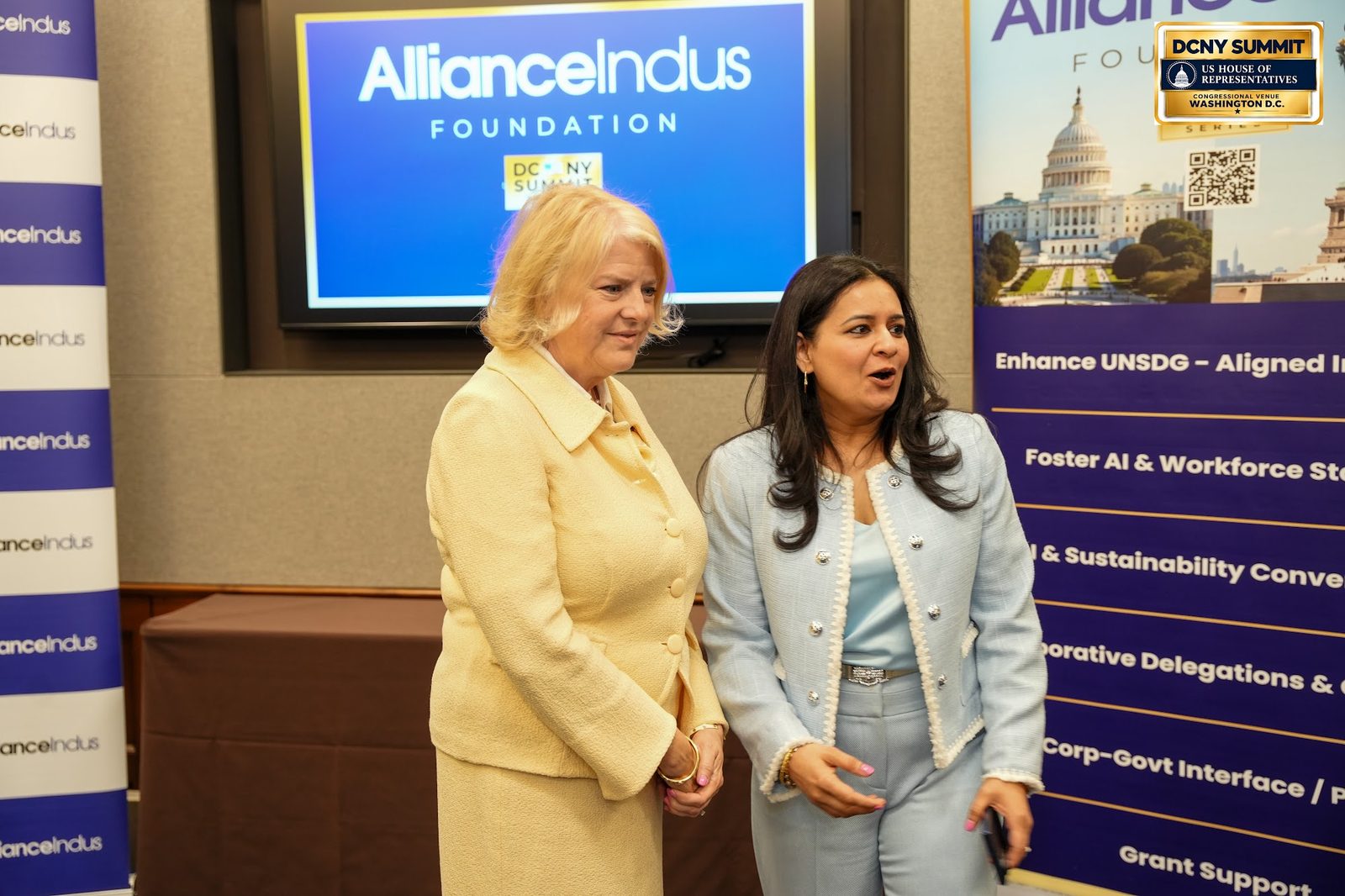Two women talking in front of a screen showing the AllianceIndus Foundation logo