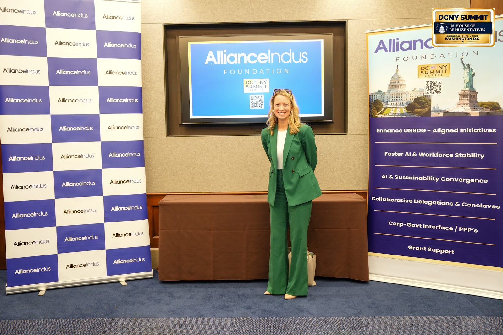A woman in a green suit poses at the AllianceIndus photo wall